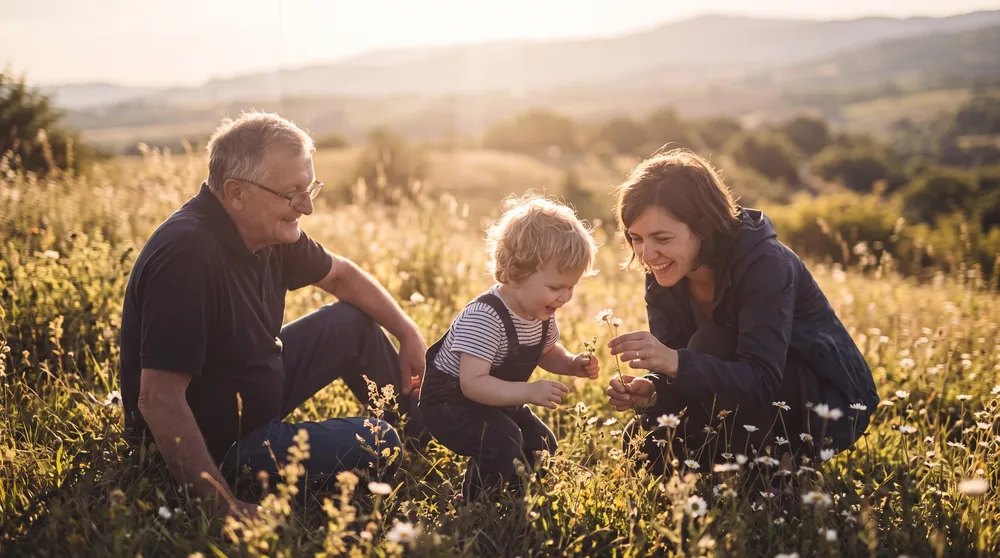 Un abuelo, una madre y un niño pequeño juegan entre flores silvestres en una colina al atardecer