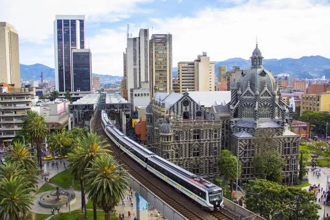 El metro de Medellín pasa junto al Palacio de la Cultura Rafael Uribe Uribe, con edificios y montañas al fondo